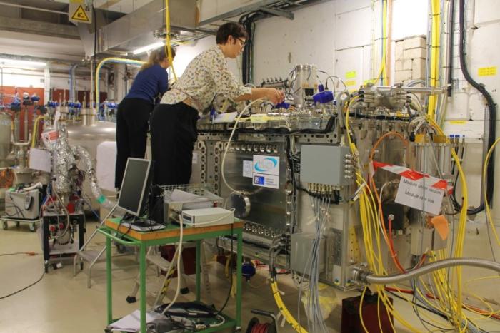 two women fixing big rectangular silver-coloured equipment with wires