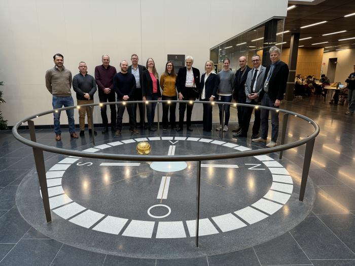 people smiling next to a circular floor compass with a hanging ball on a string