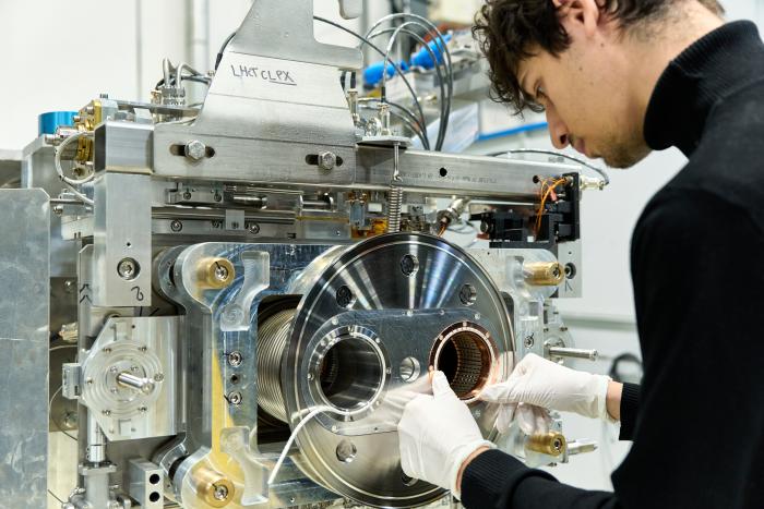 man pushing circular string-like item onto a cylindrical part of big silver equipment